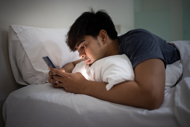 Asian young handsome man using smartphone on bed