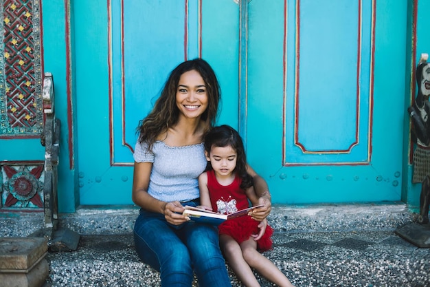 Asian young lady with book and preschool daughter smiling and looking at camera