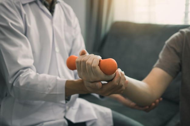 Asian young male physiotherapist helping patient with lifting dumbbells exercises in office