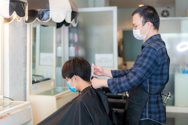 Asian young man and hairdresser man wearing medical mask to protect themselves during novel Coronavirus, Covid-19 in Barbershop Hair Care Service.
