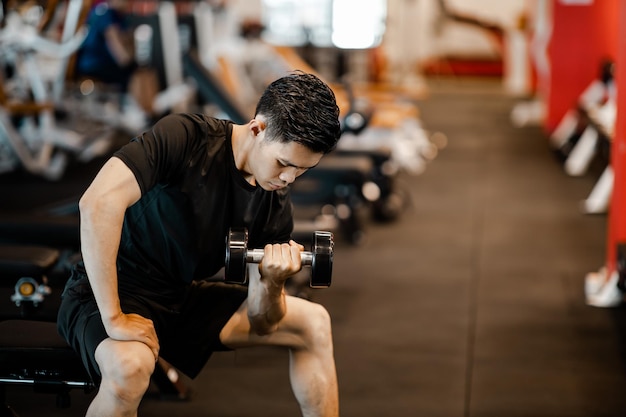 Asian young man using dumbbell exercise at gym for good healthy in fitness Lifestyle and sport exercise concept