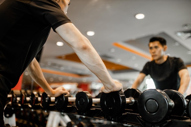 Asian young man using dumbbell exercise at gym for good healthy in fitness Lifestyle and sport exercise concept