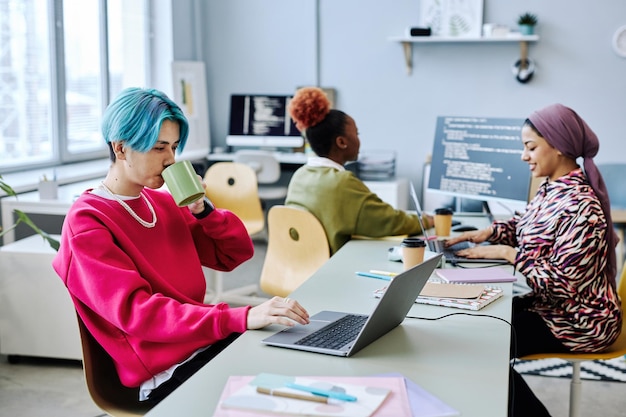 Asian young man using laptop in office and drinking coffee magenta accent