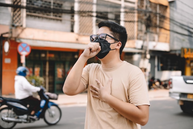 Asian young man wearing face mask to protect PM 25 protect pollution anti smog and viruses on road in the city Global warming concept Healthcare concept Environmental pollution concept