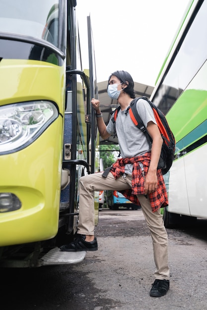 Asian young man wearing face masks getting on the bus.A man wearing a face mask and carrying a backpack gets on the bus at the terminal