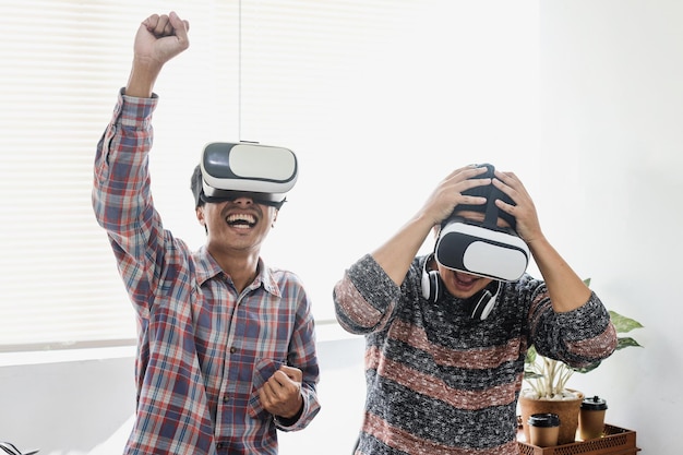 Asian young men playing games using VR glasses gesturing winning victory and loose the game.