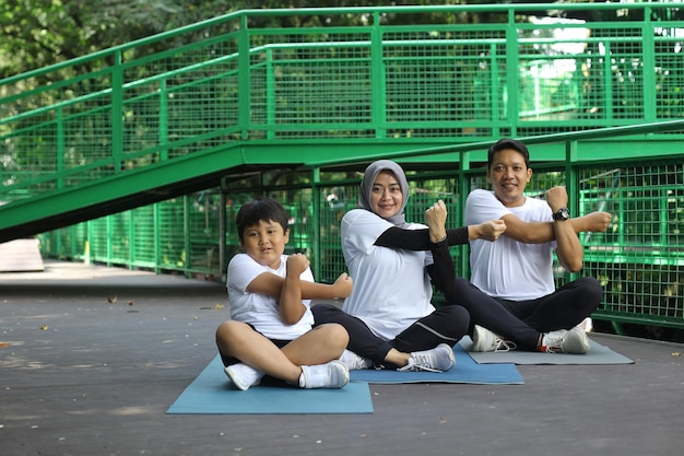 Asian young mother and father practicing yoga and stretching hand with son  at the park. Family spor