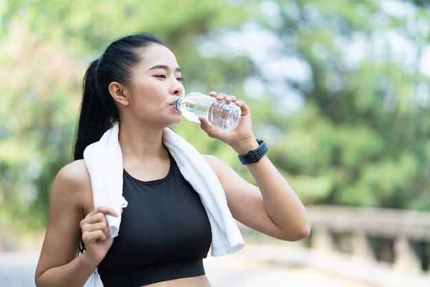 Asian young sports woman with white towel drinking water after workout exercise outdoor