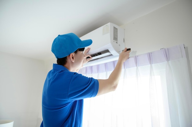 An Asian young Technician service man wearing blue uniform checking cleaning air conditioner in home