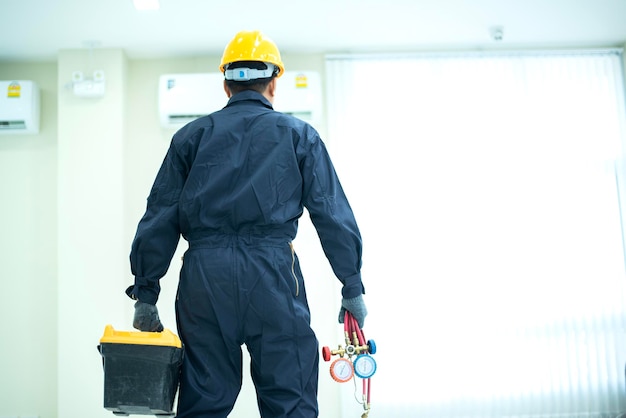 An Asian young Technician service man wearing blue uniform checkingProfessional air conditioner installer maintaining modern indoor air conditioner space for text