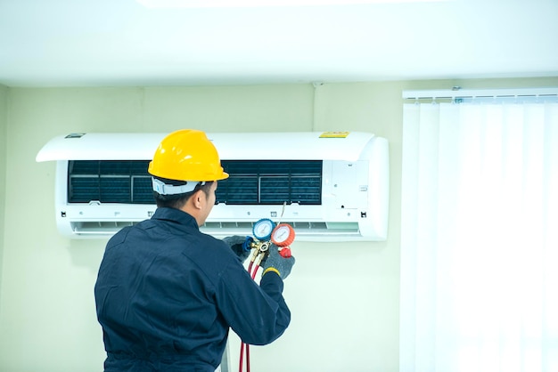 An Asian young Technician service man wearing blue uniform checkingProfessional air conditioner installer maintaining modern indoor air conditioner space for text