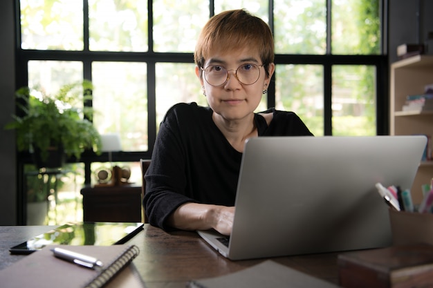 Asian young woman in casual clothing using laptop and smiling while working at home