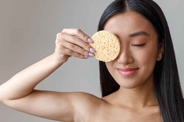 Asian young woman covering eye with cosmetic sponge