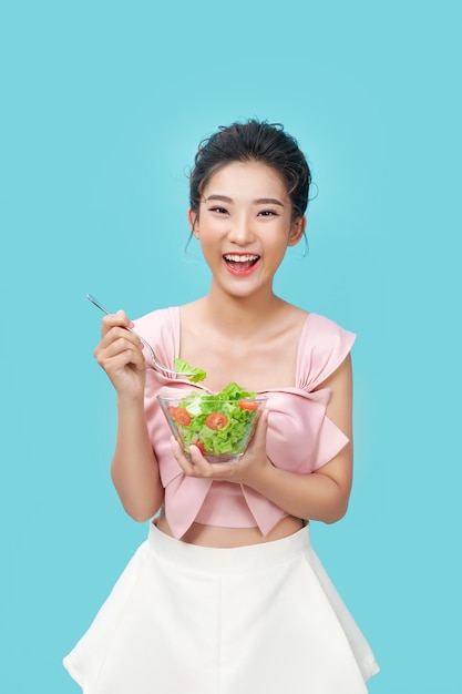 Asian young woman eatiing salad on blue background diet food concept