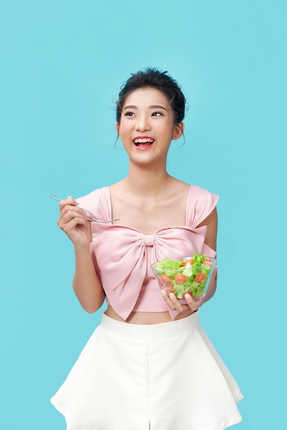 Asian young woman eatiing salad on blue background diet food concept