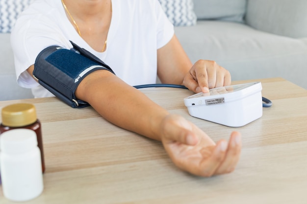 Asian young woman is checking blood pressure and heart rate with digital pressure gauge by herself at home. Health and Medical concept.