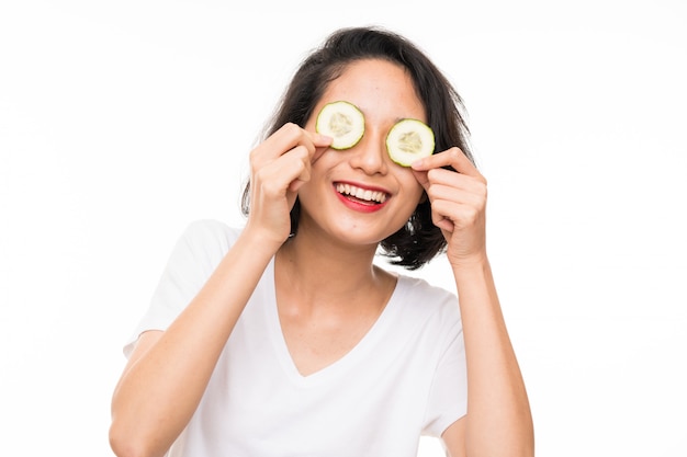 Asian young woman over isolated wall holding slices of cucumber