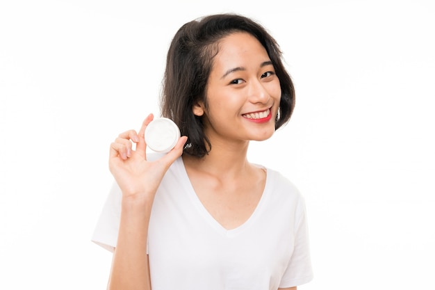 Asian young woman over isolated wall with moisturizer