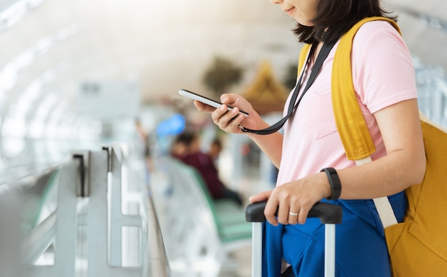 Asian young woman in pink shirt with yellow backpack is checking flight with smartphone at the airport.