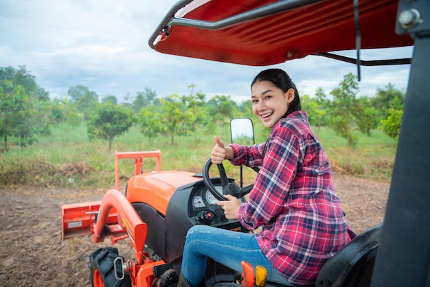 Asian young woman sitting in big tractor machine and smiling cheerfully to camera Pretty happy female farmer worker in field at farm Agricultural work