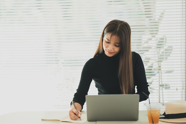 Asian young woman in smart casual wear working on laptop while sitting in creative office or cafe young girl working with laptop on the wood table in the cafe