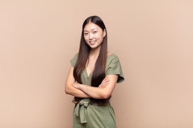 Asian young woman smiling to camera with crossed arms and a happy, confident, satisfied expression, lateral view