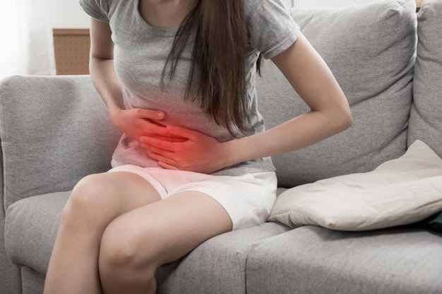 Asian young woman suffering stomach ache sitting on couch in living room at home people painful stomachache gynecology menstrual pain medical and health care concept