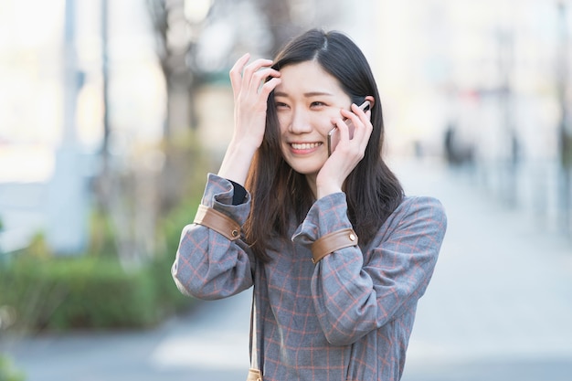 Asian young woman talking with someone with smartphone on ear