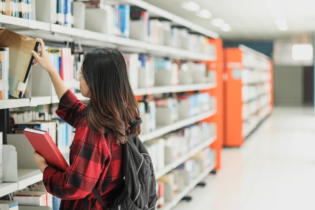 Asian young woman wearing casual style and backpack is picking a book on bookshelf at the library.