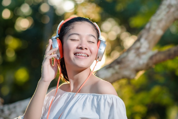 asian young woman with headphones and listening music on sunset in park.