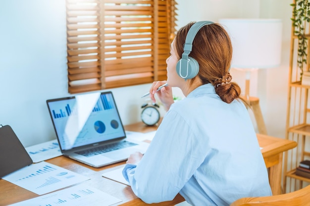 Asian young woman working from home using computer and drinking coffee in her room document finance and conference online meeting for new projects