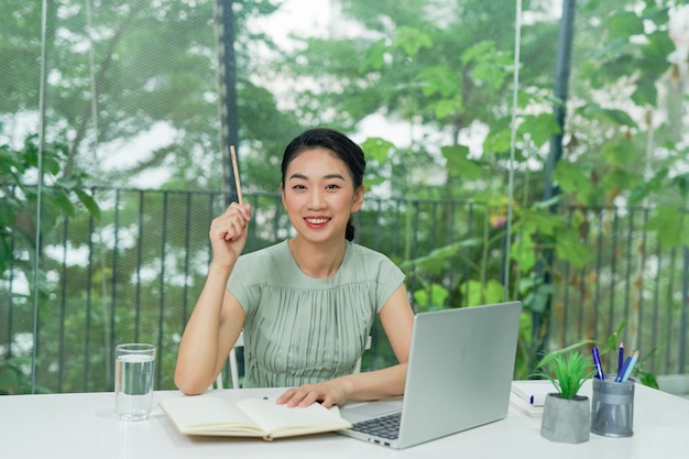 Asian young woman working with computer laptop holding pen and thinking to get ideas and requirement