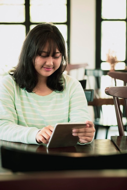 Asian younger woman reading message on computer tablet with smiling face