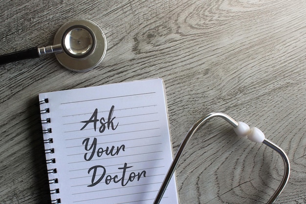 Ask your doctor on notebook with stethoscope on wooden background Medical and healthcare concept