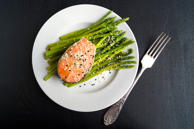 Asparagus with salmon on a white plate. On a black background.