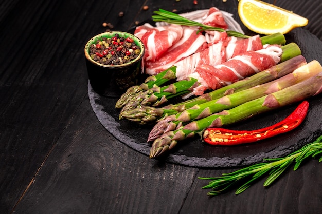 Asparagus wrapped in fatty bacon ham on a slate board top view Food recipe background