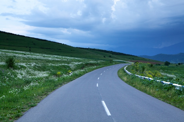 Asphalt road goes down the mountainside in the forest in the evening