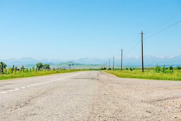 Asphalt road and green fields with mountains under the blue sky