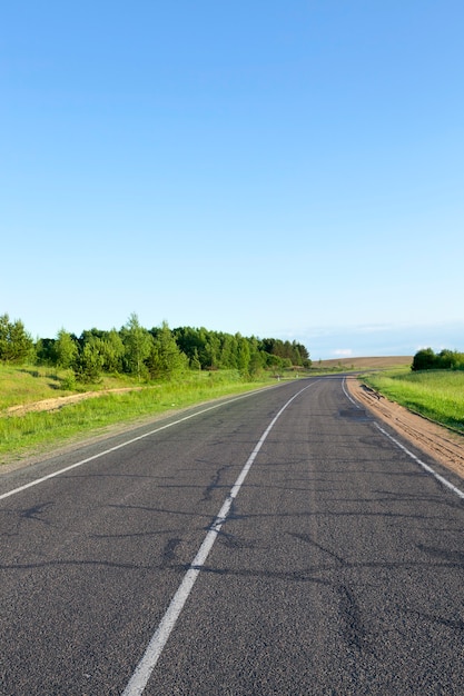 Asphalt road in summer, landscape with green grass and blue sky