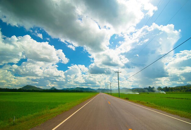 asphalt road through the green field and clouds on blue sky in summer