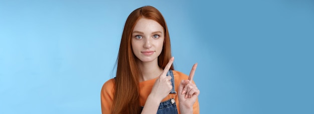 Photo assertive goodlooking redhead girl know what talking about pointing upper left corner index fingers