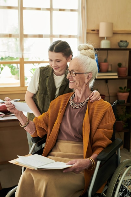 Photo assisting elderly caucasian woman in wheelchair indoors