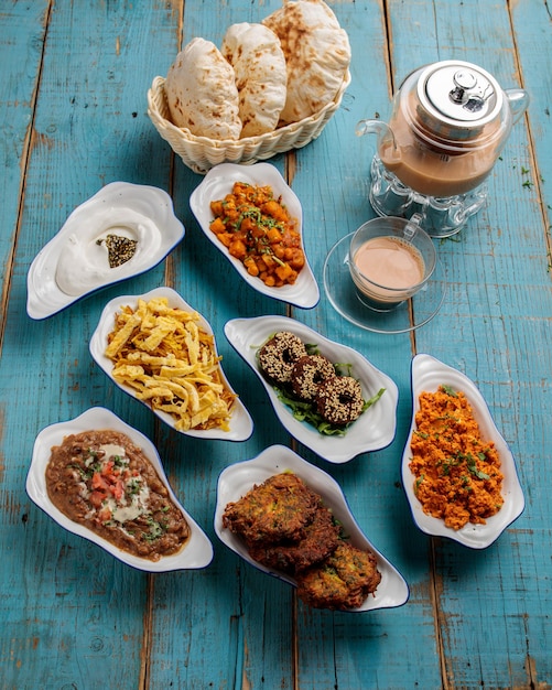 Assorted bahraini breakfast set table with bread coffee tea kababs donut vegetables isolated on wooden table side view