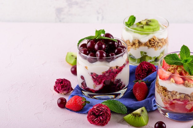 Assorted berries desserts on a pink table, three glasses with different desserts of granola, whipped cream, strawberries, kiwi, cherries