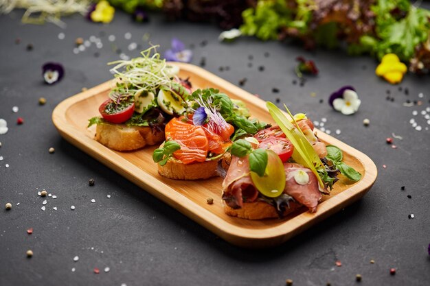 Assorted bruschetta set with salmon parma and pesto souce Italian antipasti snacks Variety mix of small sandwiches on dark background Photo for restaurant menu