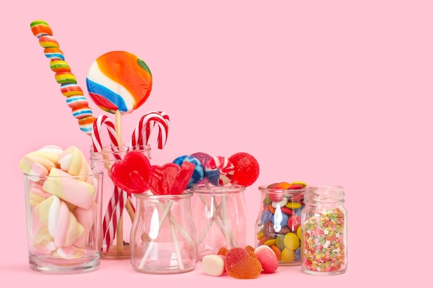 Assorted candies and lollipops in crystal jars on a pink background