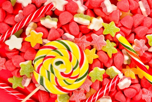 Assorted colorful gummy candies and lollipop on red background Top view Jelly sweets