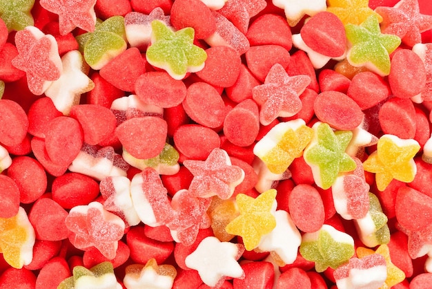 Assorted colorful gummy candies and lollipop on red background Top view Jelly sweets