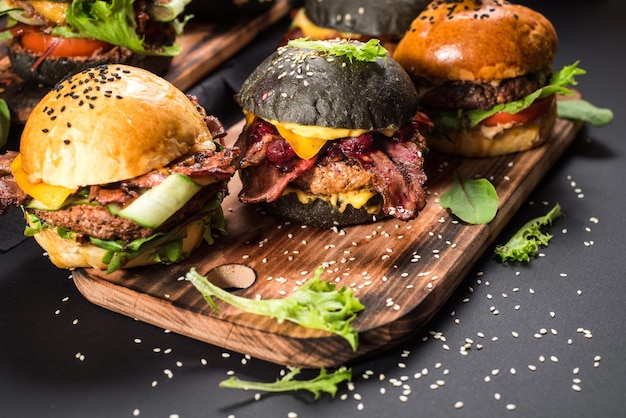 Assorted craft burgers with different fillings, with sesame seeds on the black background