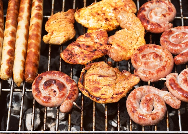 Assorted delicious grilled meat over the hot fire on a portable barbecue with steaks sausages